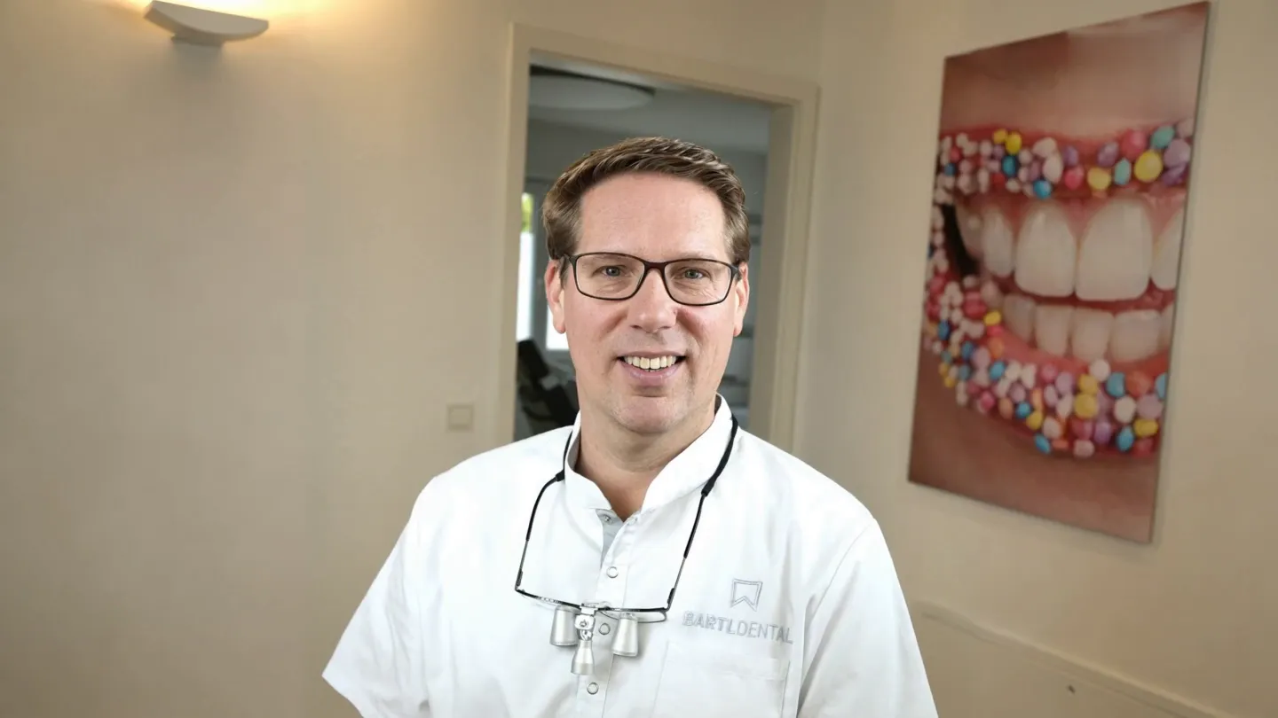 Zahnarzt M.Sc. Robert Bartl lächelnd im hellen Flur seiner Praxis in Bobingen, neben dem Bild mit dem Lächeln (Foto vom Shooting, mit KI zum Breitbild erweitert; Anfang des Films)