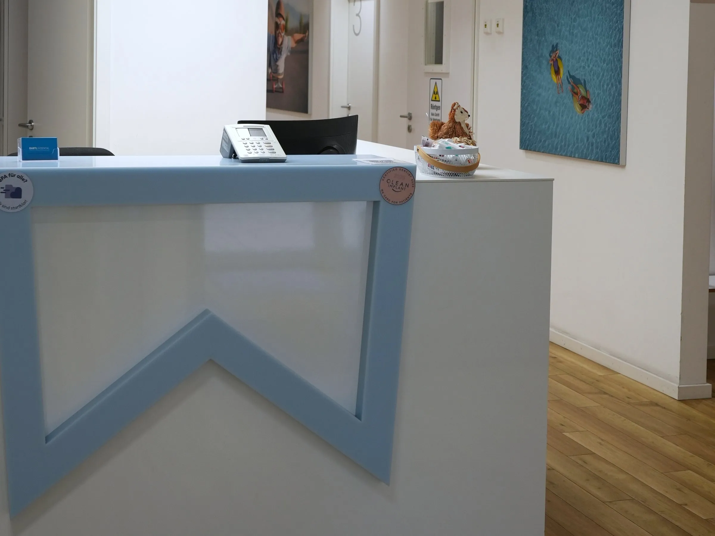 Empfang: weißer Tresen mit hellblauem Zickzack-Rahmen, dahinter Türen, rechts ein großes blaues Wandbild